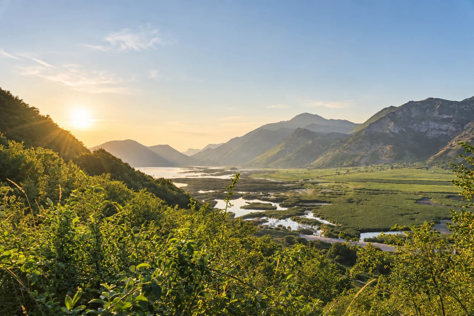 Il sole tramonta sulla piana del lago, tra canneti e montagne